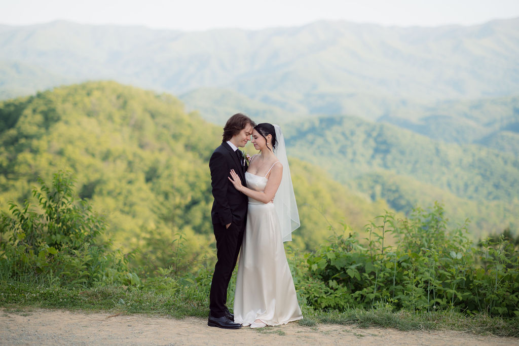 Newlyweds stand forehead to forehead at a mountain overlook, surrounded by green Smoky Mountain ridges while eloping to Gatlinburg.