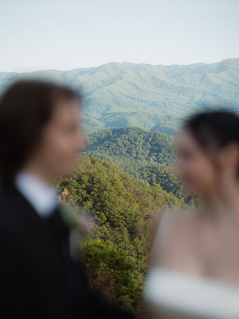 Great Smoky Mountains fill the frame between an out-of-focus bride and groom during their Foothills Parkway elopement portraits.