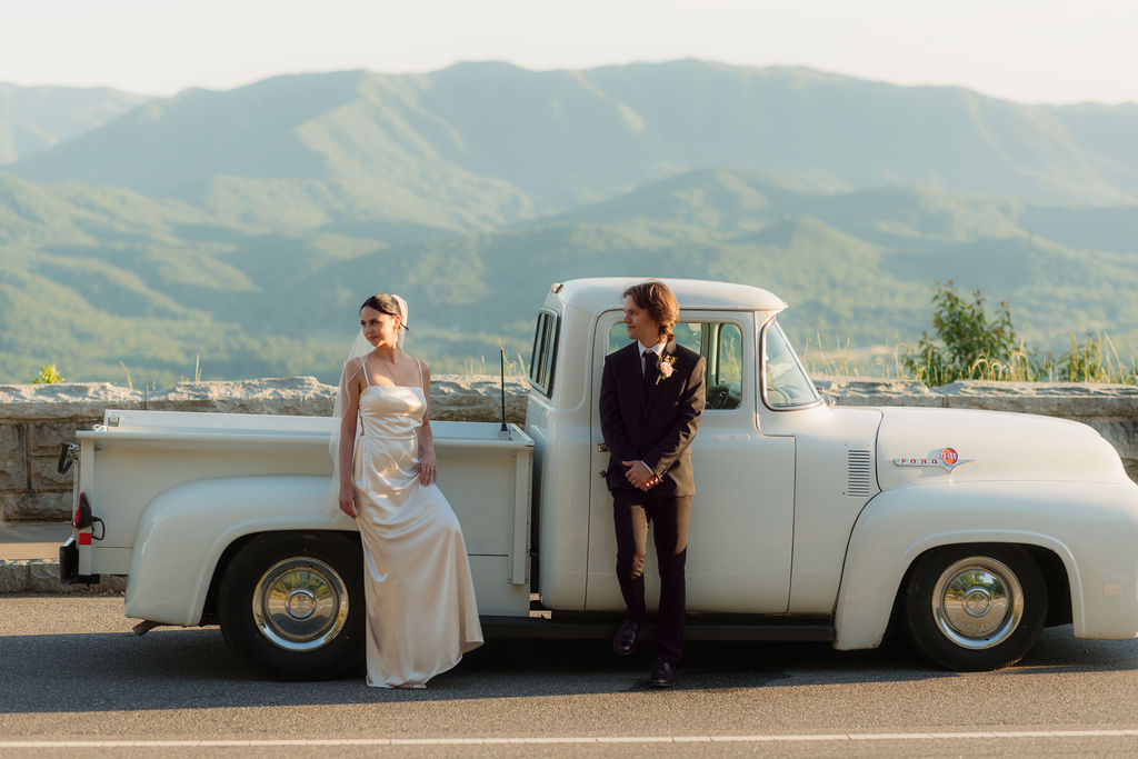 Bride and groom pose beside a vintage white pickup truck with layered Smoky Mountain views during a Foothills Parkway elopement.