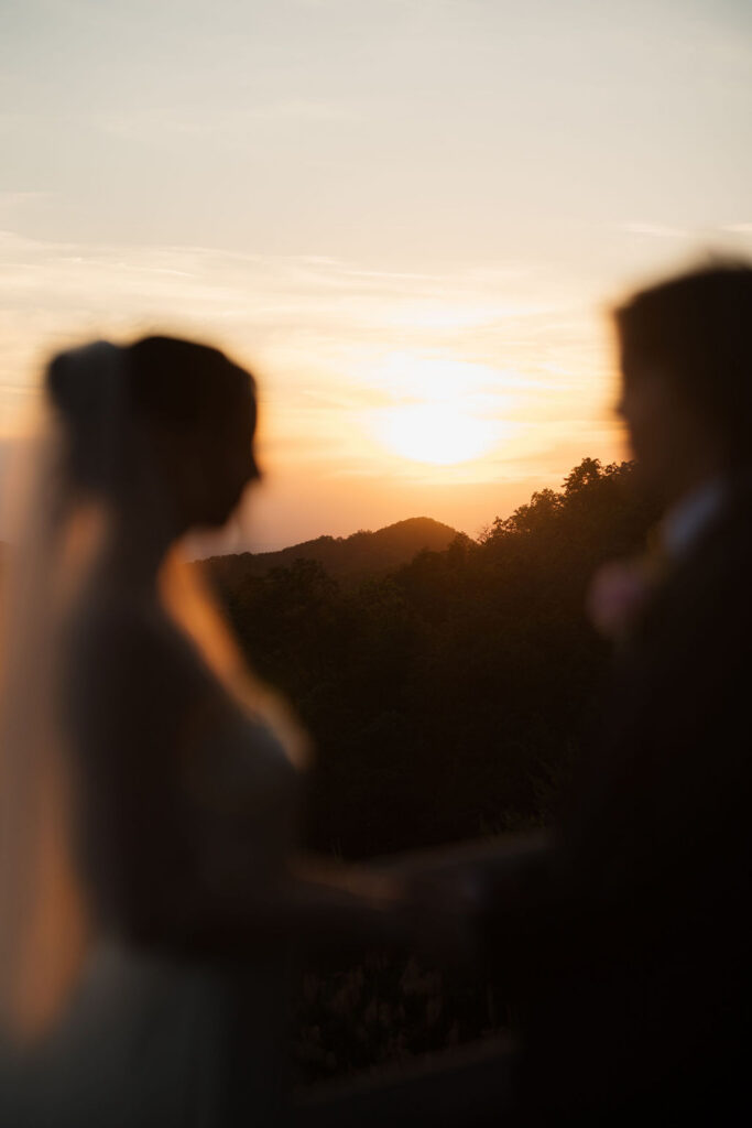 Soft-focus silhouettes of newlyweds frame the orange mountain sunset, creating a scenic detail from their Foothills Parkway photos.