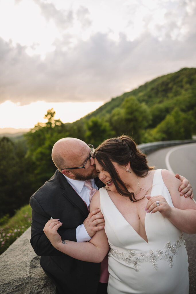 Groom kisses the bride's forehead beside Foothills Parkway, capturing a joyful and intimate moment while eloping to Gatlinburg.