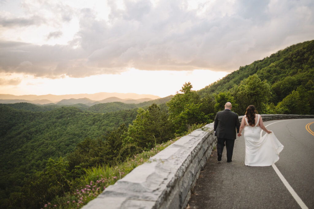 Bride and groom walk hand in hand along Foothills Parkway at sunset, with sweeping Smoky Mountain views showcasing the beauty of eloping to Gatlinburg.
