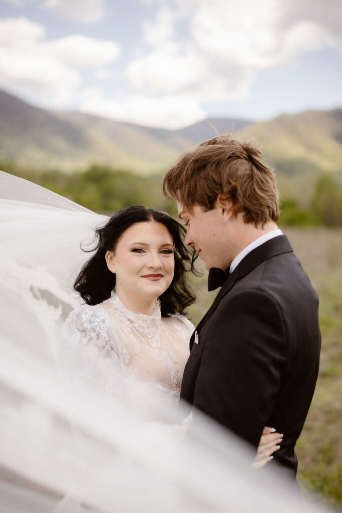 Bride and groom share a romantic portrait beneath a flowing veil in Cades Cove, capturing the intimate moments of eloping to Gatlinburg.