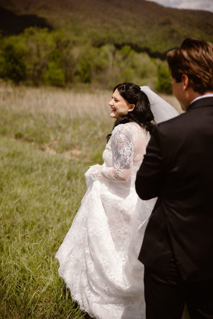 Bride smiles while walking through the open fields of Cades Cove with her groom, showcasing the peaceful experience of eloping to Gatlinburg.