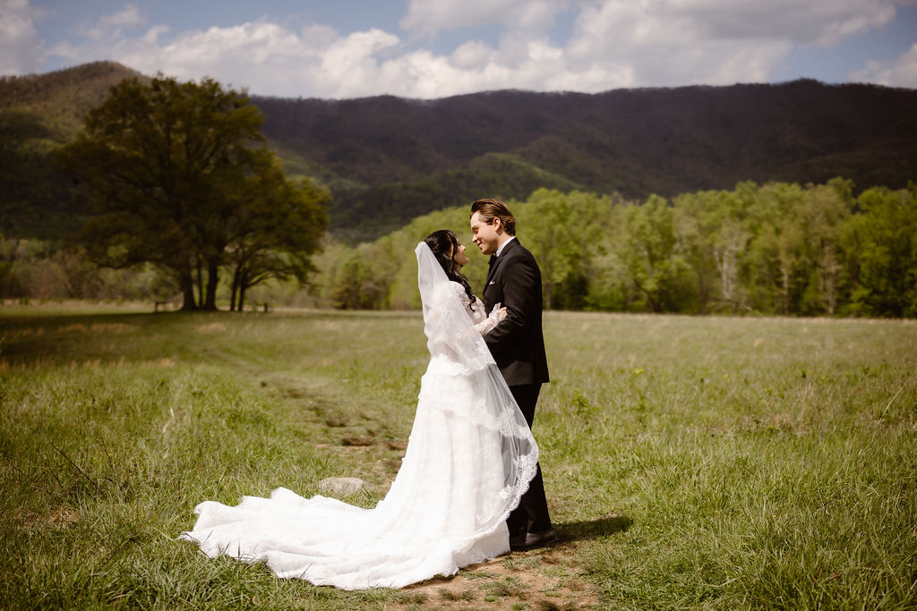 Bride and groom embrace in the open fields of Cades Cove with the Smoky Mountains behind them, highlighting the beauty of eloping to Gatlinburg.