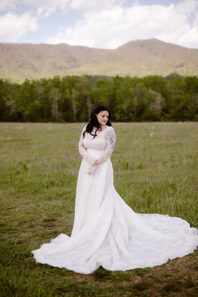 Bride stands in a flowing lace wedding dress in the open fields of Cades Cove, showcasing the natural beauty of eloping to Gatlinburg.