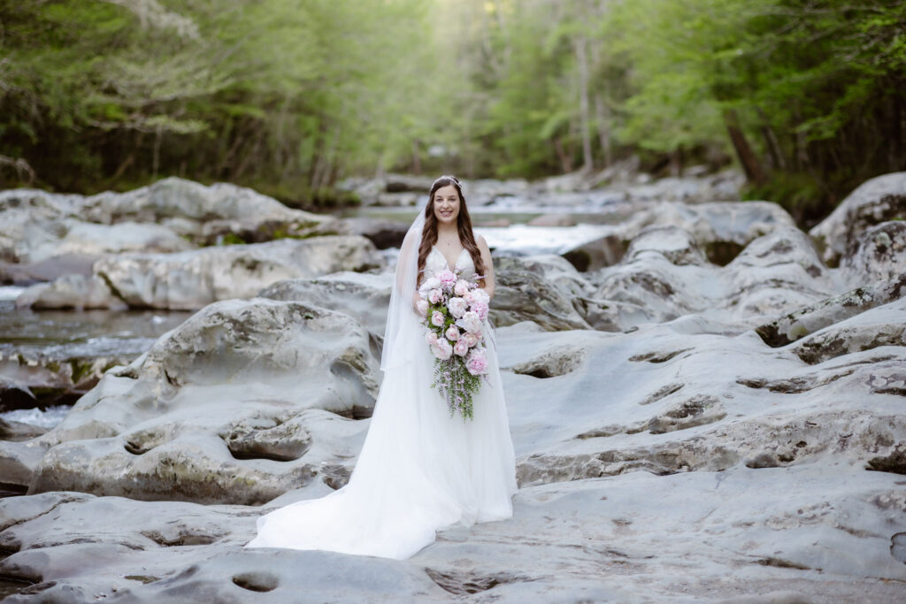 Bride stands among smooth river rocks with a cascading floral bouquet during an intimate great smoky mountain national park wedding.