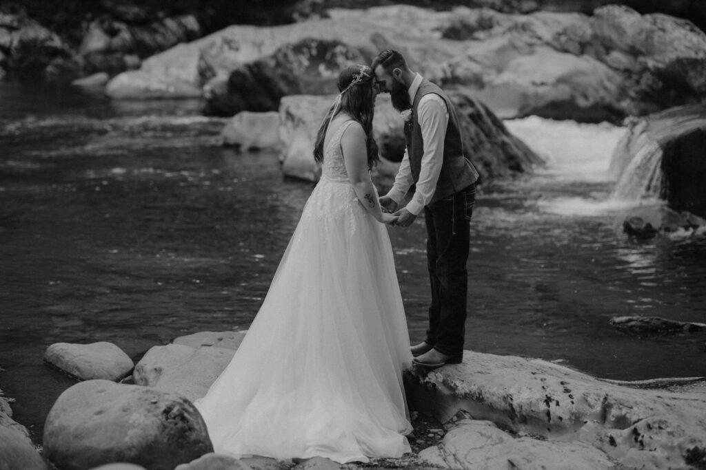 Black-and-white portrait of newlyweds holding hands beside flowing water while eloping to gatlinburg.