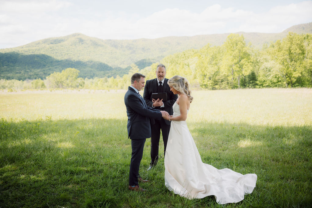 Couple exchanges vows with their officiant in a grassy mountain meadow, photographed by an elopement photographer during an intimate Gatlinburg wedding ceremony.