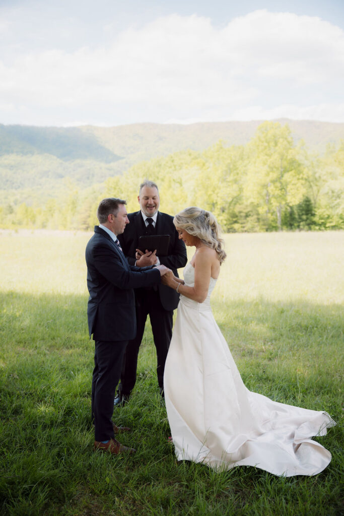 Couple holds hands with their officiant during a Gatlinburg Elopement Ceremony, surrounded by a sunny meadow and sweeping Smoky Mountain views.