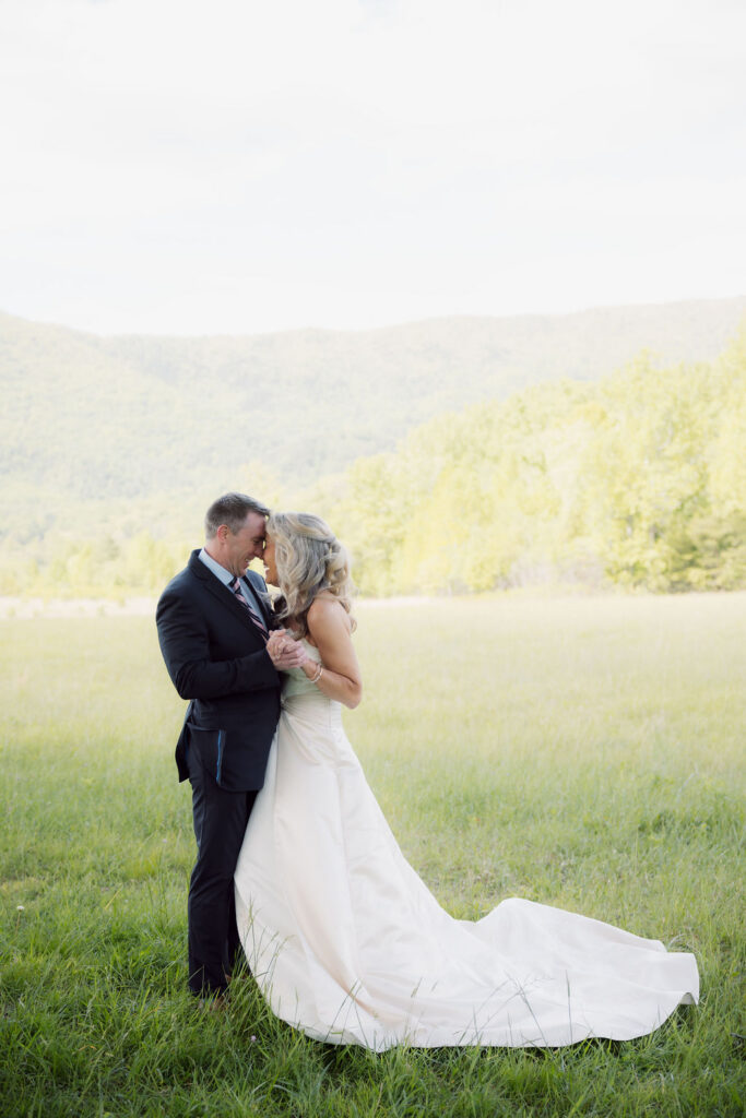 Newlyweds stand forehead to forehead in a sunlit meadow after their cades cove elopement, surrounded by expansive Smoky Mountain scenery.
