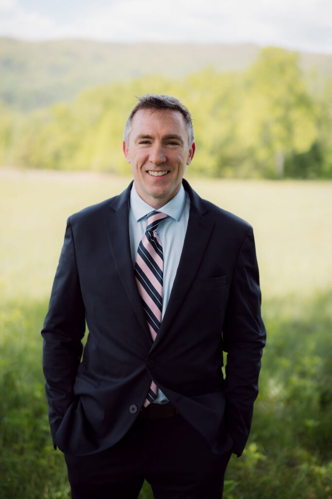 Groom portrait in a mountain meadow while eloping to gatlinburg, with soft green forest and Smoky Mountain scenery in the background.