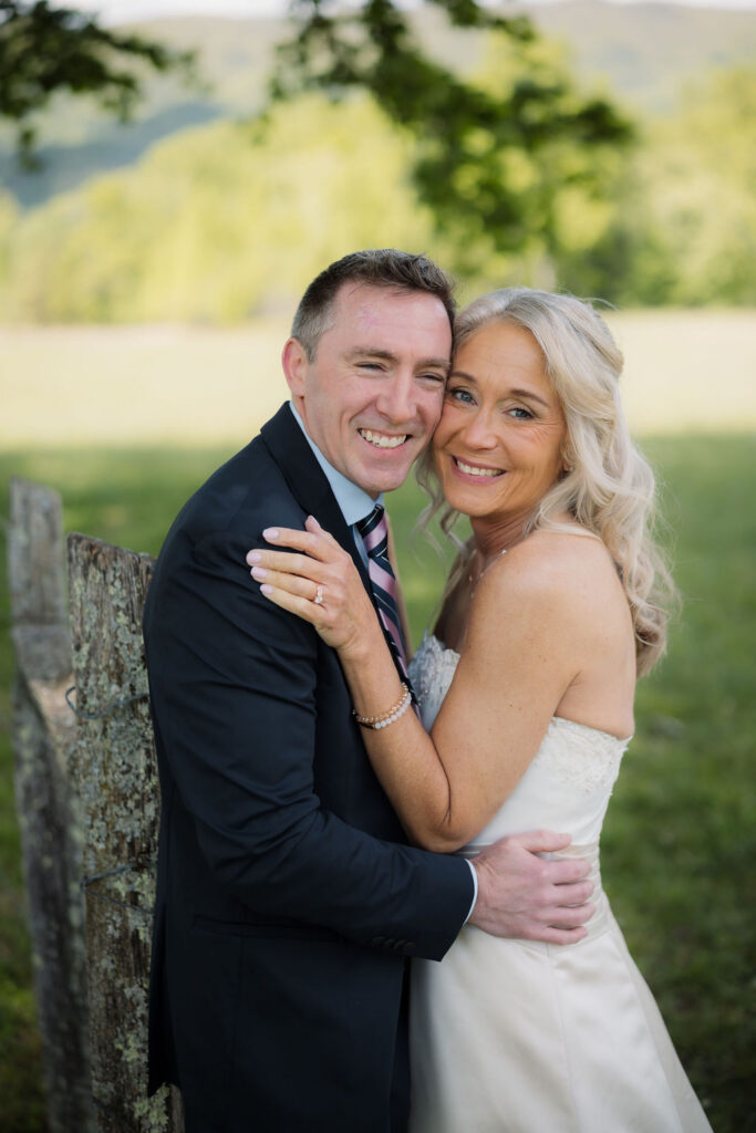 Newlyweds pose together beside a weathered wooden fence during their cades cove elopement, with soft mountain scenery in the distance.
