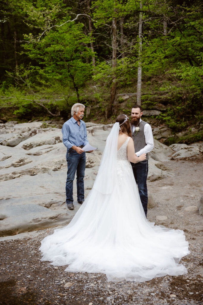 Bride and groom stand with their officiant on a rocky riverbank surrounded by spring forest during an intimate gatlinburg elopement.