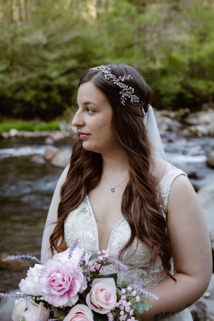 Close-up bridal portrait with jeweled hairpiece, veil, and pink bouquet beside the river in greenbrier.