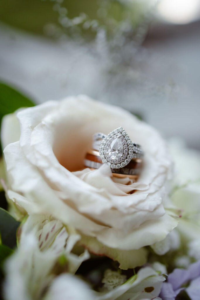 Pear-shaped diamond engagement ring and wedding bands nestled inside a white rose for a gatlinburg elopement in the Smoky Mountains.