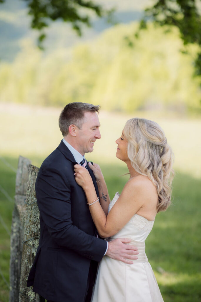 Newlyweds embrace beside a rustic fence after their cades cove elopement, captured by a gatlinburg photographer with mountain scenery behind them.