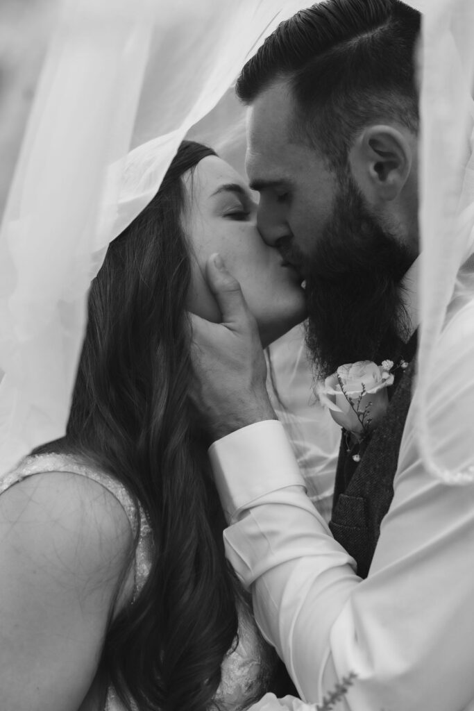 Black-and-white portrait of newlyweds kissing beneath the bride’s veil, an intimate moment captured while visiting the smokies for their wedding.