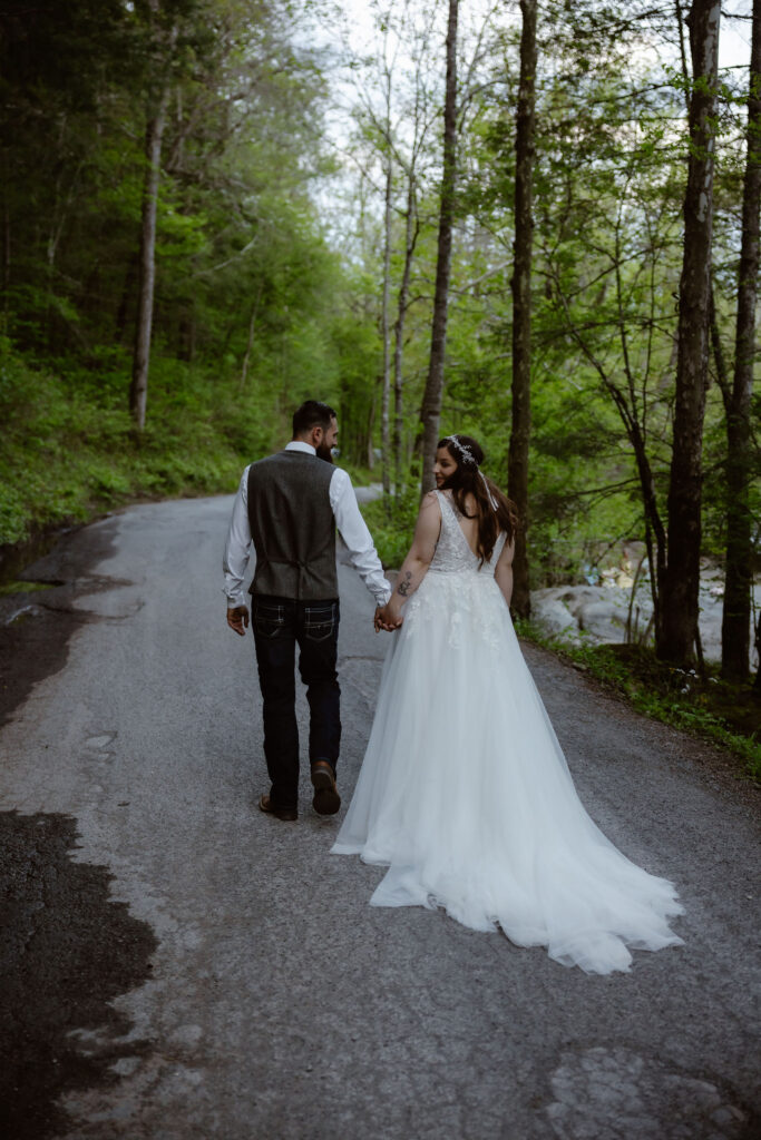 Newlyweds walk hand in hand along a quiet forest road after their wedding while visiting the smokies.