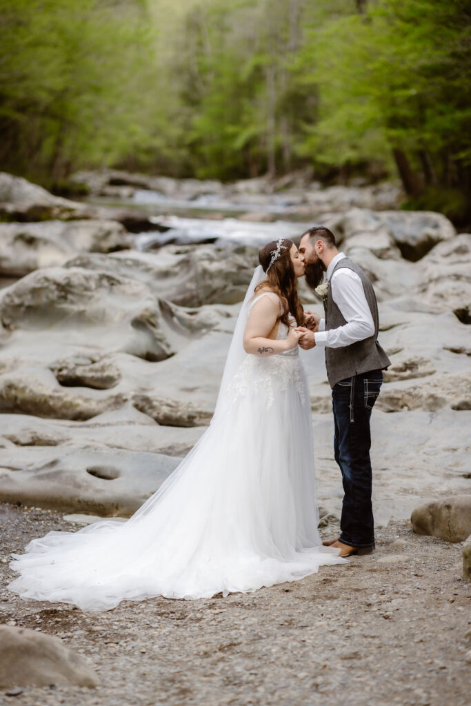 Bride and groom kiss beside a rocky mountain stream during their waterfall elopement in greenbrier.