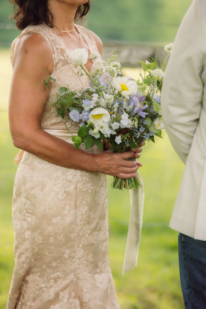 Close-up of a bride in a champagne lace wedding dress holding a wildflower bouquet of white, blue, and lavender blooms during her smoky mountain elopement.