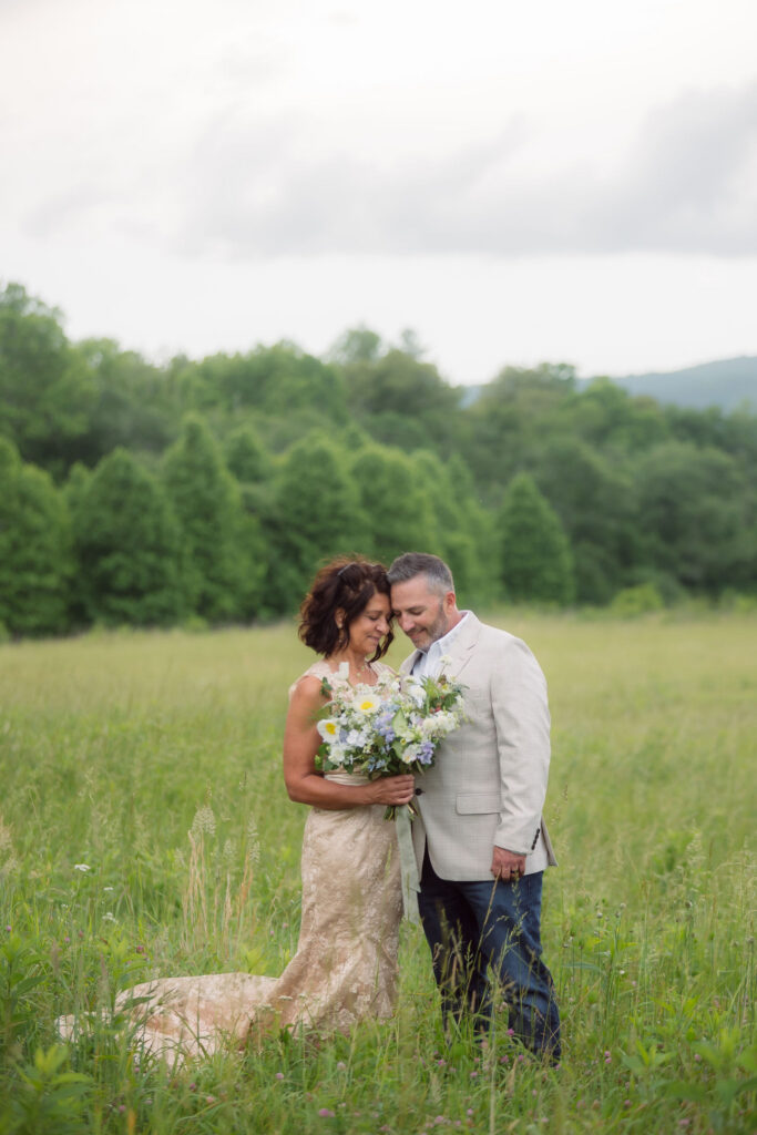 Bride and groom rest their foreheads together in a grassy meadow, holding a pastel wildflower bouquet during their gatlinburg elopement.